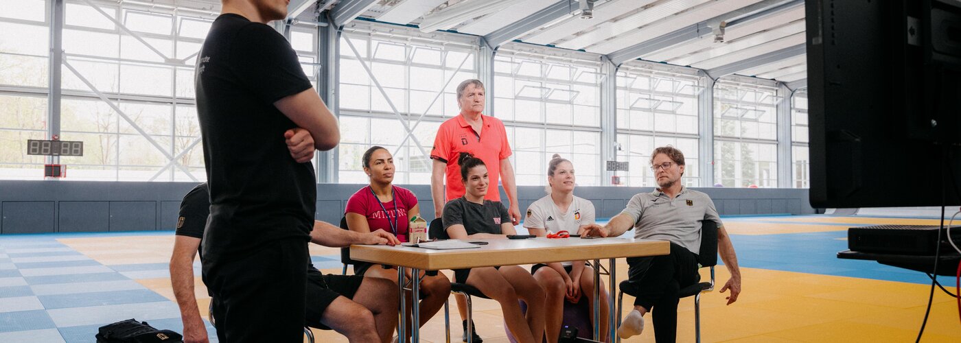 Ein IAT-Wissenschaftler, DJB-Bundestrainer, Athletinnen und Trainerteam besprechen am Monitor Taktikempfehlungen für den Wettkampf